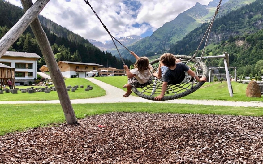 Kids on swing with mountains in the back at the South Tyrolean Nature Resort